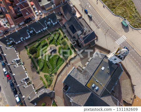 Aerial view of a compact town centered on a white facade church with dome and clock tower, surrounded by cobblestone streets, red and gray roofed buildings, green spaces, and parked cars. 131192609