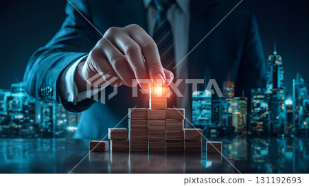 Businessman's hand stacking glowing blocks against the background of a city with buildings Businessman's hand stacking glowing blocks against the background of a city with buildings 131192693