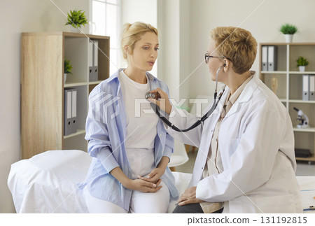 Doctor performing chest auscultation with stethoscope on female patient in clinic 131192815