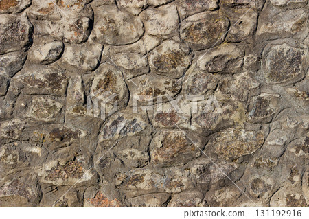 Old stone wall with irregular natural rocks set in mortar. Weathered textures, earthy tones, rough patterns, ideal for background, design element in architectural, historical, rustic-themed designs 131192916