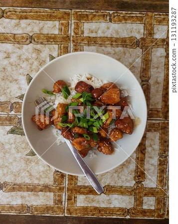 Homemade Teriyaki chicken with sesame and scallions over white rice, plate with fork on tile table. Mobile photography, real phone snapshot 131193287