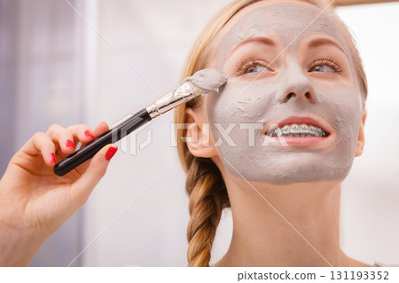 Woman applying with brush clay mud mask to her face Woman applying with brush clay mud mask to her face 131193352