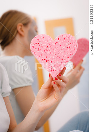 Woman having grey face mask holding heart sponge 131193355