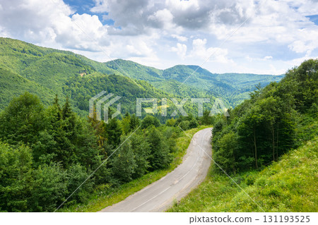 road through mountain landscape in summer. scenic view from above. green nature scenery in dappled light under cloudy sky. beautiful valley with pass winding between forest 131193525