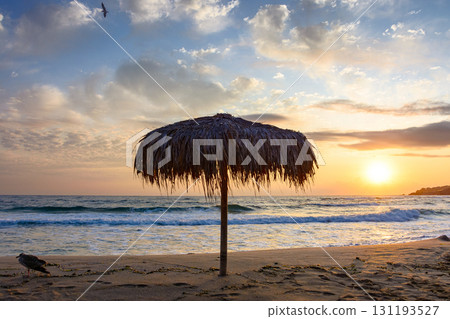 umbrella on the sand beach at sunrise. summer vacation at the sea. blue sky with glowing clouds. beautiful landscape for travel with sun above horizon. tranquil scenery in orange light 131193527