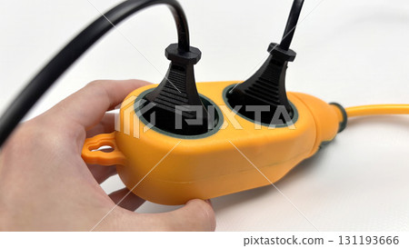 Hand holding outdoor waterproof orange power extension socket, portable heavy duty electrical splitter for garden, camping, construction or workshop, close-up isolated on white background Hand holding outdoor waterproof orange power extension socket, portable heavy duty electrical splitter for garden, camping, construction or workshop, close-up isolated on white background 131193666