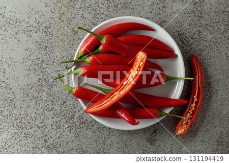 Fresh red chili peppers with green stems on a gray stone table. 131194419