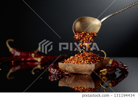 Dry red chili peppers and crushed chili flakes on a black reflective background. 131194434