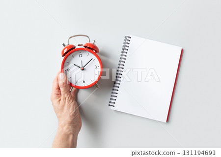 Alarm clock in woman hand and empty sheet blank on gray background. View from above. Copy space. 131194691