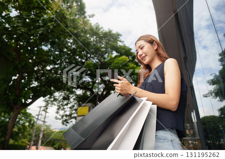 Shopping and Technology. Young woman using smartphone while holding shopping bags. Shopping and Technology. Young woman using smartphone while holding shopping bags. 131195262