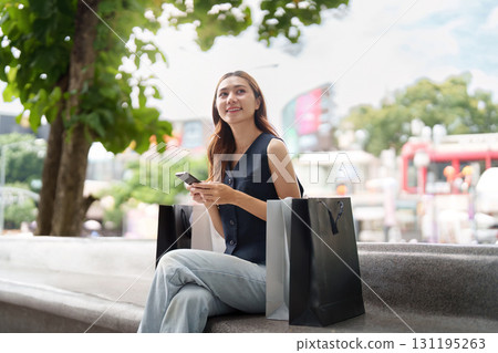 Relaxed Shopping. Young woman sitting on a bench with shopping bags and smartphone. Relaxed Shopping. Young woman sitting on a bench with shopping bags and smartphone. 131195263