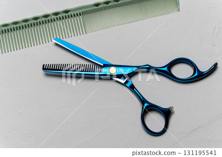 Blue thinning scissors and hair comb on grey surface Blue thinning scissors and hair comb on grey surface 131195541