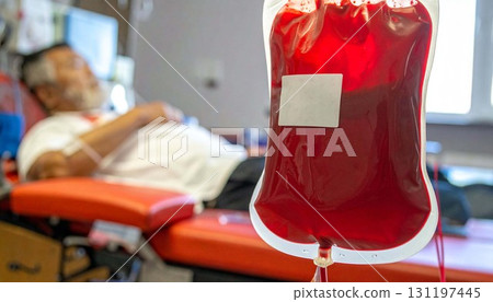 Blood collection bag for donation rests on a stand with a donor reclining during a donation event in a medical facility Blood collection bag for donation rests on a stand with a donor reclining during a donation event in a medical facility 131197445