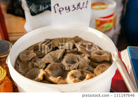 Inscription on the price tag: Grusdi - means Milk mushrooms: Altai pickled mushrooms in a plastic bucket at the fair 131197646