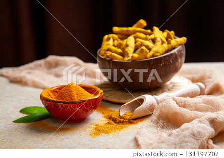 Dried turmeric roots in coconut shell bowl and powder with leaves Dried turmeric roots in coconut shell bowl and powder with leaves 131197702