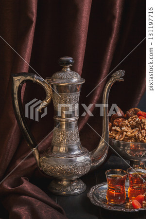 Still life with Ancient East crockery - jug for water or tea, vase with dried fruit and plate with tea in armuda glasses 131197716