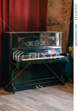 Old vintage piano stands in the hall against the background of a red curtain and a brick wall 131197837