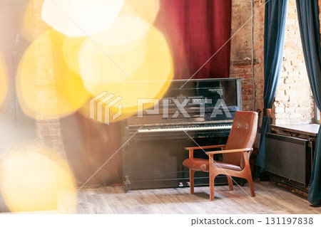 Old vintage piano and armchair stands in the hall against the background of a red curtain and a brick wall near the big window, with bokeh and highlights 131197838