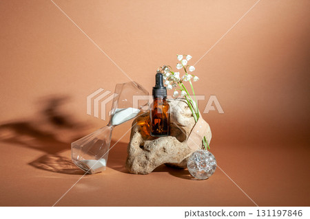 Modern still life with serum bottle on background of unusual natural stone, with bouquet of lilies of the valley and hourglass. The concept of anti-aging care products 131197846