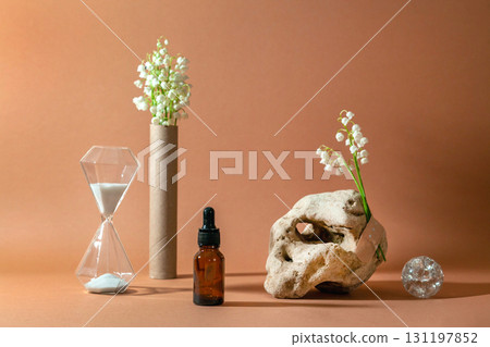 Modern still life with serum bottle on background of unusual natural stone, with bouquet of lilies of the valley and hourglass. The concept of anti-aging care products 131197852