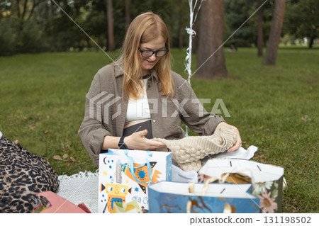 Pregnant woman opening baby shower gifts at outdoor celebration Pregnant woman opening baby shower gifts at outdoor celebration 131198502