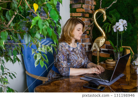 A young woman interior designer is working in her office at a computer. Green office, live plants in an office space A young woman interior designer is working in her office at a computer. Green office, live plants in an office space 131198946