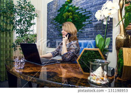 A young woman interior designer is working and talking on the phone in her office at a computer. A young woman interior designer is working and talking on the phone in her office at a computer. 131198953