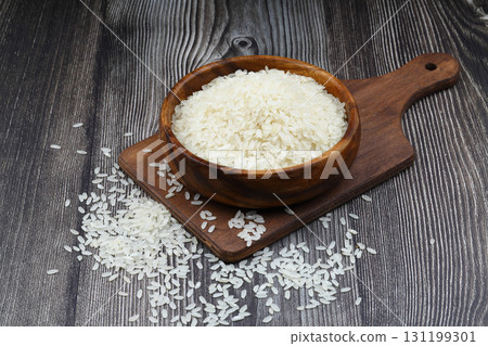 Raw white rice on wooden background. Long uncooked rice in wooden plate. Natural organic food. Traditional Asian cereal culture. Raw white rice on wooden background. Long uncooked rice in wooden plate. Natural organic food. Traditional Asian cereal culture. 131199301