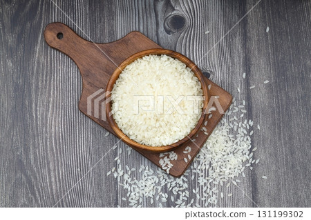 Raw white rice on wooden background. Long uncooked rice in wooden plate. Natural organic food. Traditional Asian cereal culture. Raw white rice on wooden background. Long uncooked rice in wooden plate. Natural organic food. Traditional Asian cereal culture. 131199302