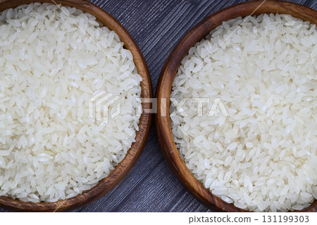 Raw white rice on wooden background. Long uncooked rice in wooden plate. Natural organic food. Traditional Asian cereal culture. 131199303