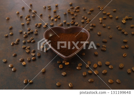 Roasted coffee beans in heart shaped bowl on dark background. Love coffee concept. Top view flat lay Roasted coffee beans in heart shaped bowl on dark background. Love coffee concept. Top view flat lay 131199648