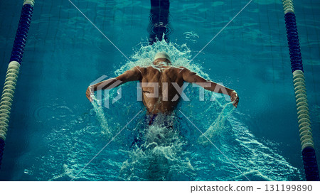 Male swimmer butterfly stroke seen from behind creating splash in pool 131199890