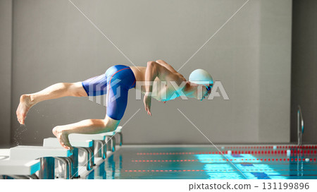 Swimmer in streamlined dive motion launching into pool from starting block 131199896