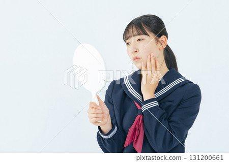 身穿水手服的女學生一邊看著手鏡裡的自己,一邊擔心 身穿水手服的女學生一邊看著手鏡裡的自己,一邊擔心 131200661