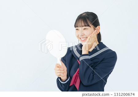 A female student wearing a sailor suit looking at a hand mirror with a smile 131200674