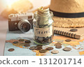 A travel fund is being saved in a jar with a map, camera, and hat nearby.. 131201714