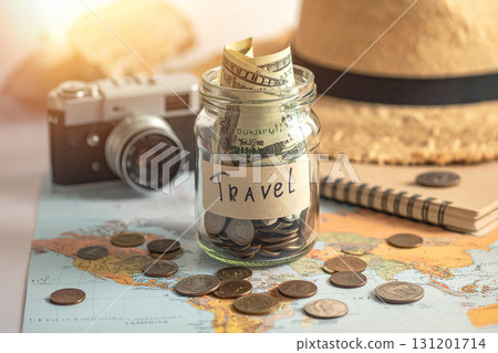 A travel fund is being saved in a jar with a map, camera, and hat nearby.. 131201714