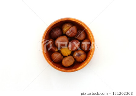 Peeled sweet chestnuts served on a wooden plate on a white background, viewed from directly above 131202368