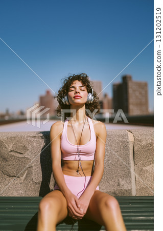 A woman wearing headphones and a pink bikini is sitting on a bench 131202519