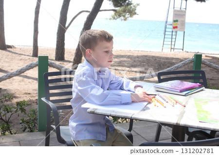 little cute boy with workbook doing homework on table outside in cafe, lifestyle people concept 131202781