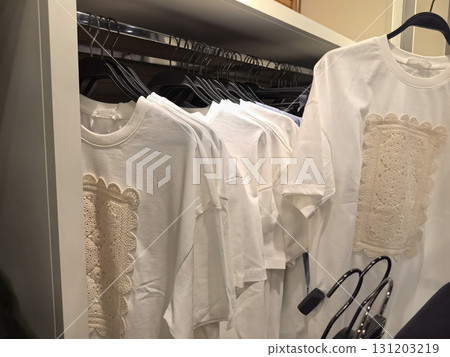 Trendy white t-shirts with elegant lace details hanging in a boutique Trendy white t-shirts with elegant lace details hanging in a boutique 131203219