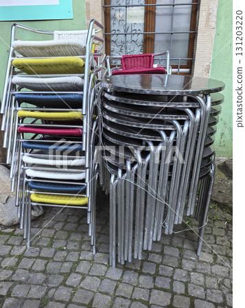 Colorful stacked chairs and a round table resting on cobblestone street Colorful stacked chairs and a round table resting on cobblestone street 131203220