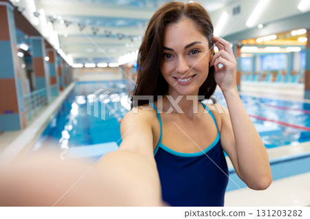 Slim dark-haired young woman in one-piece swimsuit looking happy while making selfie Slim dark-haired young woman in one-piece swimsuit looking happy while making selfie 131203282