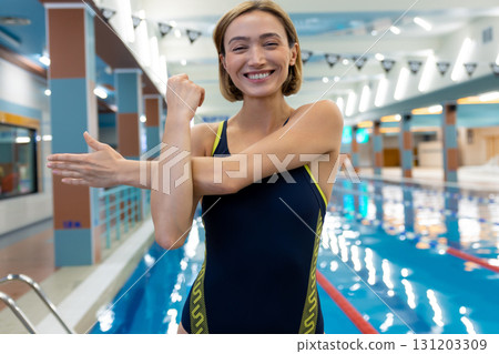 Positive slim short-haired woman doing warming up exercises before swimming in the pool 131203309