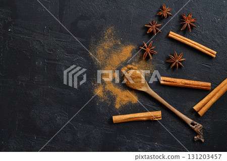 Aromatic cinnamon sticks, cinnamon powder and anise on black table, flat lay. Space for text 131203457