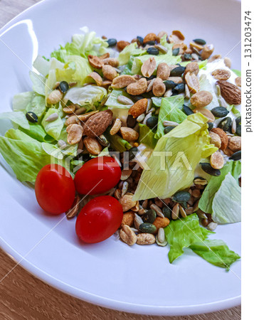 Fresh salad with lettuce, seeds, nuts and cherry tomatoes. Fresh vegetable salad with lettuce, cherry tomatoes, nuts and seeds on a white plate. Includes a small portion of buckwheat for extra texture 131203474