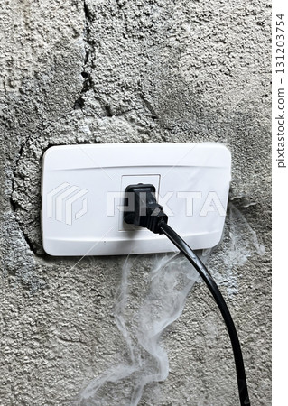 A smoking electrical outlet on a gray concrete wall from overvoltage, short circuit cause of fire A smoking electrical outlet on a gray concrete wall from overvoltage, short circuit cause of fire 131203754