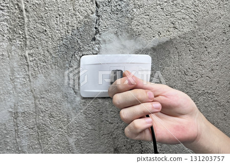 A smoking electrical outlet, a hand pulling the plug out of a burning outlet 131203757