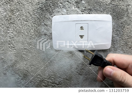 A smoking electrical outlet, a hand pulling the plug out of a burning outlet A smoking electrical outlet, a hand pulling the plug out of a burning outlet 131203759