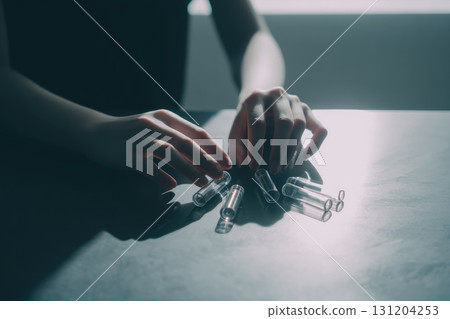 Hands arranging transparent glass vials on gray table in soft natural light, creating calm and focused atmosphere, with minimalist and clinical style 131204253